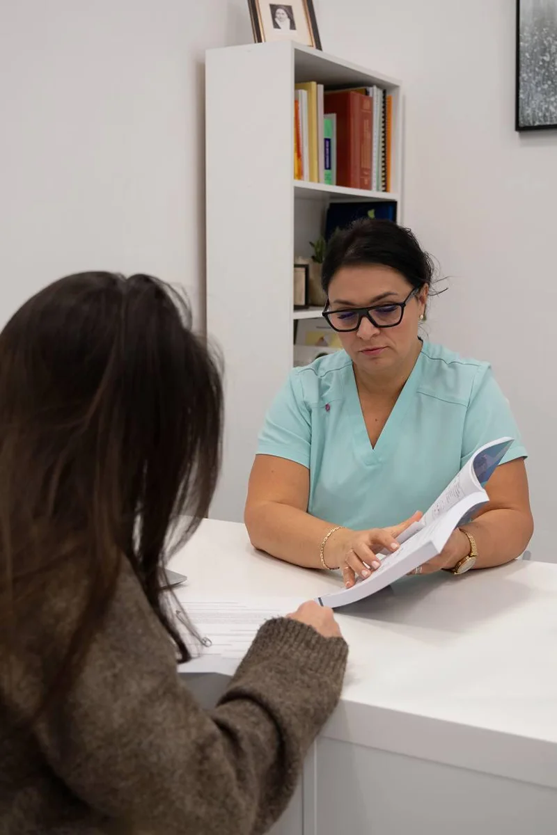 dr hab Oksana Samoiliuk za biurkiem pokazuje coś pacjentce